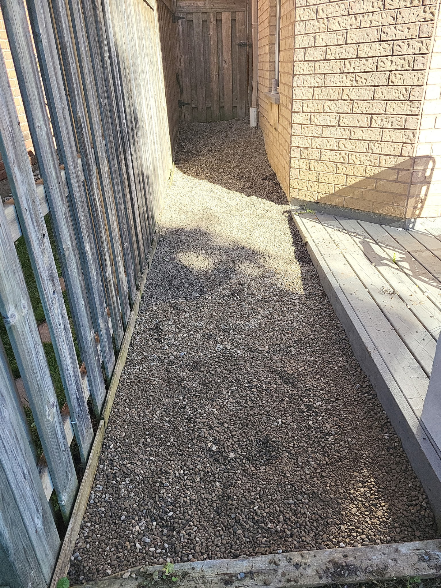 Finished gravel side-yard installation beside a backyard deck