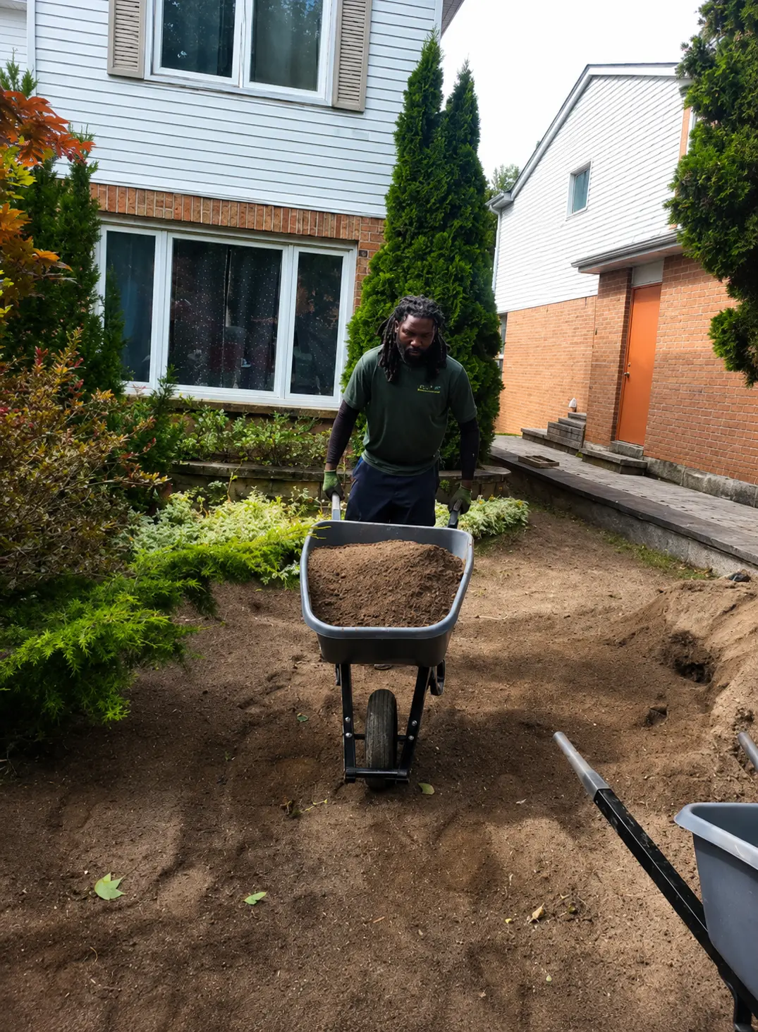 Damion moving soil by wheelbarrow on a front-yard job site